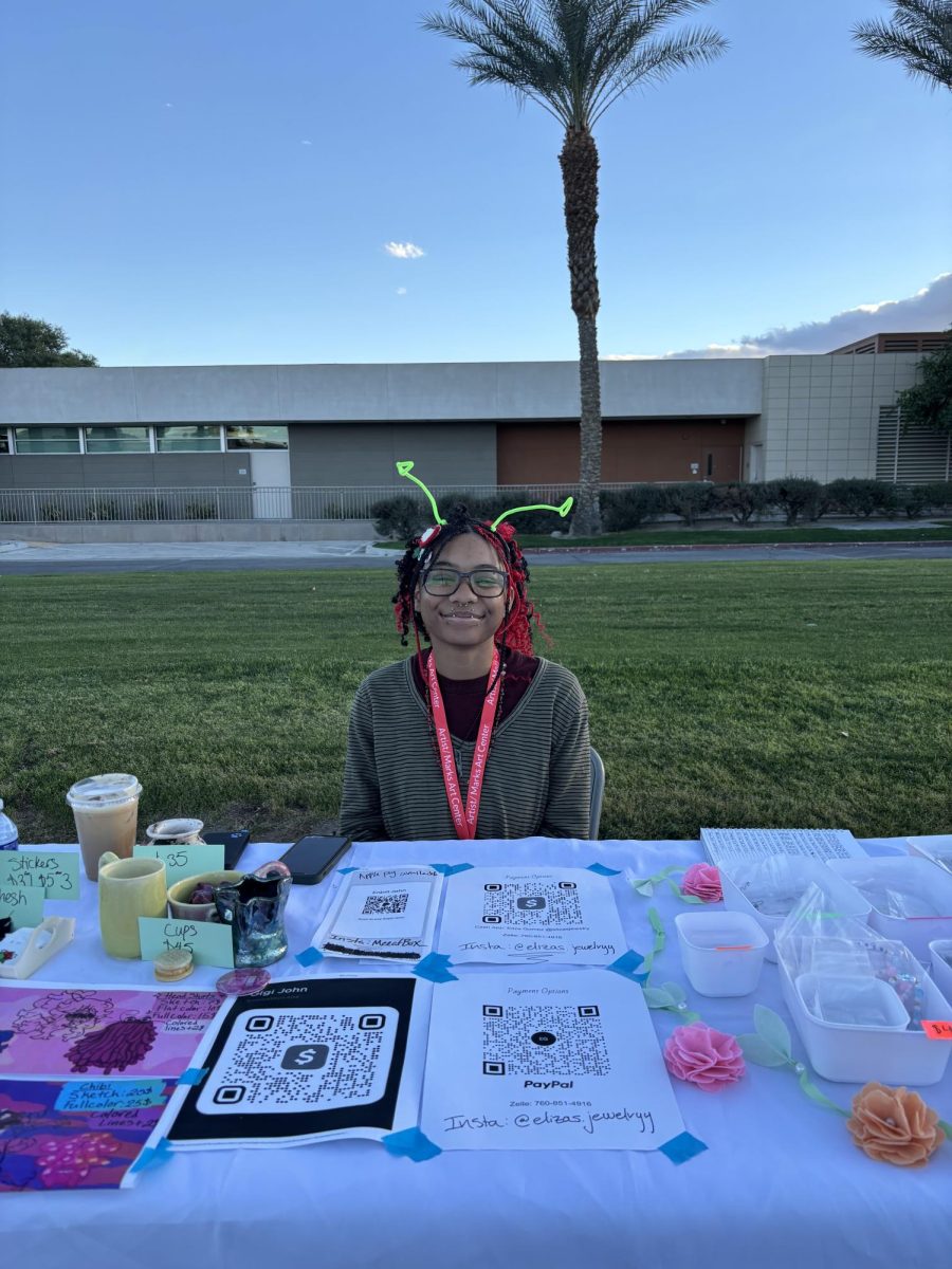 Photo courtesy of The Chaparral/Layla Freiberg. Gigi John poses in front of his booth at the art market.