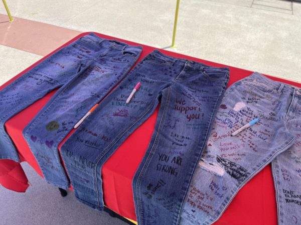 Three pairs of blue jeans on a table. There are Sharpie markers on them and students have written words of encouragment all over the jeans, such as "We support you!" and "It's never your fault."